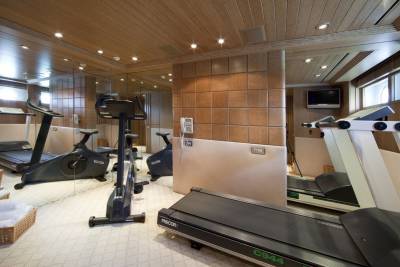 This luxurious yacht gym features multiple treadmills and stationary bikes, all set against a backdrop of polished wood and mirrored walls.