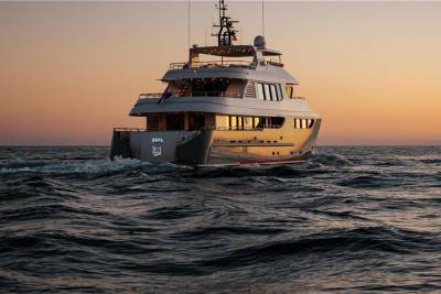 A sleek yacht glides through choppy waters at sunset, its windows reflecting the warm, golden light.