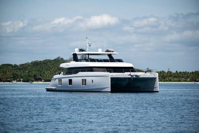 A sleek, modern catamaran glides through calm blue waters near a tropical island paradise.