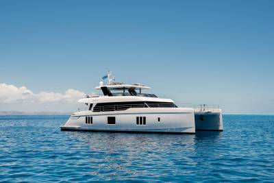 A sleek white catamaran glides across the tranquil turquoise waters under a clear blue sky.