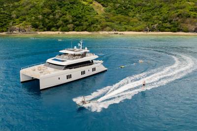 A luxurious catamaran anchors near a lush tropical island as people enjoy water sports in the crystal-clear blue ocean.
