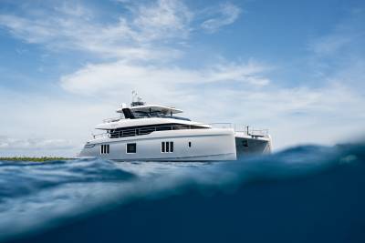 A sleek, modern catamaran glides through turquoise waters near a lush, tropical island under a bright blue sky.
