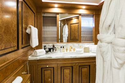 Luxurious white bathrobes hang in a richly paneled bathroom with a marble vanity and gold fixtures.