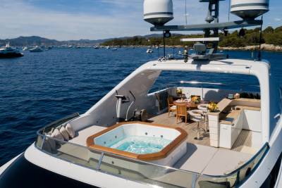 A luxurious yacht features a bubbling hot tub and elegant outdoor dining area set against a backdrop of a serene, boat-filled bay.
