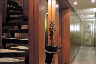 A striking spiral staircase crafted from dark wood and textured risers leads into a hallway with warm wood paneling and elegant lighting.