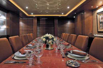 A formal dining room aboard a luxury yacht features a long table set for a feast with elegant place settings and a floral centerpiece.