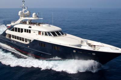 A sleek, dark blue yacht cuts through the deep blue ocean, leaving a frothy white wake in its path.
