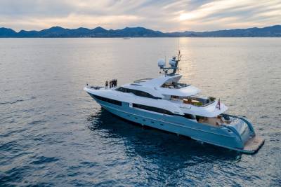 A luxurious yacht cruises on calm waters against a backdrop of distant mountains and a soft sunset sky.