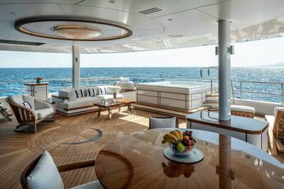 Luxurious yacht deck offers a serene oasis with a hot tub, plush seating, and a fruit-laden dining table overlooking the sparkling ocean.