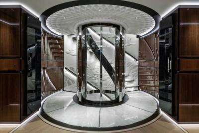 A luxurious yacht interior features a stunning glass elevator surrounded by intricately carved walls and rich wood paneling.