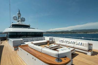 Luxurious white sofas and coffee tables create a stunning outdoor lounge on the deck of a yacht against a backdrop of the azure sea and distant hills.