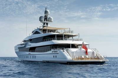 A luxurious white yacht glides across the calm blue ocean under a partly cloudy sky.