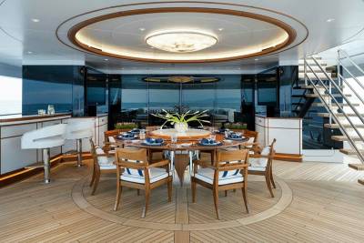 Elegant dining chairs surround a circular table set for a meal on a yacht's polished wooden deck.