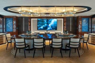 A luxurious oval dining table is set for a formal meal beneath a stunning modern chandelier.