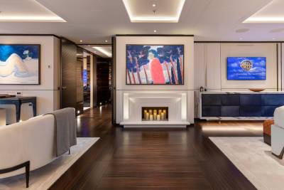 A luxurious yacht living room features modern art, a sleek fireplace with candles, and a large screen displaying the Warner Bros. logo.