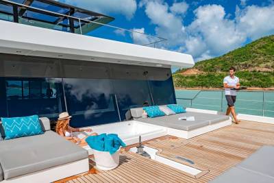 A woman relaxes in a yacht's jacuzzi while a server delivers cocktails on a sunny day.