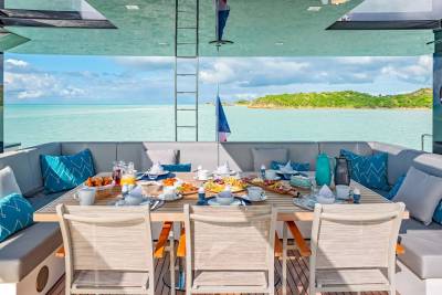 A beautifully set table awaits a delightful breakfast on a yacht deck, overlooking a serene turquoise ocean and lush green islands.
