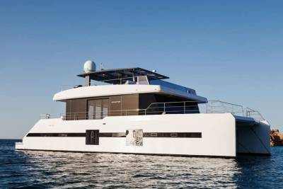 A sleek white catamaran glides through calm blue waters under a clear sky.