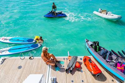 A group enjoys a sunny day of water sports from a luxurious yacht, with jet skis, paddleboards, and a kayak ready for adventure.
