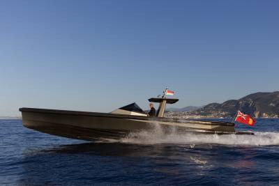 A sleek, modern boat cuts through the azure waters with a man at the helm and flags flying proudly.