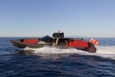 A sleek, dark boat with bright red seating speeds through the deep blue ocean under a clear sky.