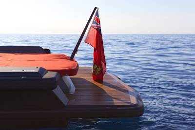 A red ensign flutters from a yacht's stern as it glides across the calm blue sea.