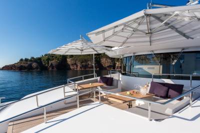 Two elegant umbrellas shade a luxurious yacht deck, offering a perfect spot to enjoy drinks and the stunning coastal scenery.