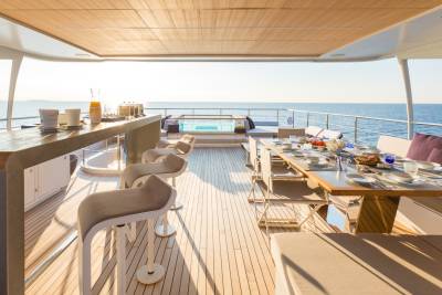 A luxurious yacht deck offers a stunning dining experience with a table set for a meal and a refreshing dip in the jacuzzi.