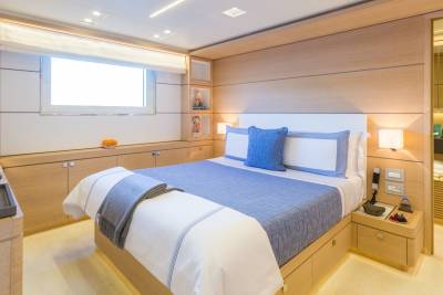 A serene bedroom aboard a yacht features a comfortable bed with blue accents and a large window offering bright natural light.