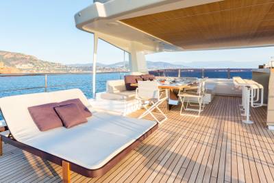 Relax on the sun-drenched deck of a luxury yacht, with a dining area and bar overlooking the sparkling blue sea.