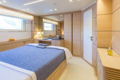 A tranquil bedroom aboard a luxury yacht features a comfortable bed, ample storage, and a well-lit vanity area.