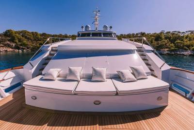 Luxurious white cushions and pillows adorn the deck of a yacht anchored near a lush, tree-covered coastline.