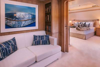 A luxurious yacht cabin features a comfortable white sofa, a framed ocean view, and a glimpse into a serene bedroom.
