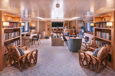 Relax in this luxurious yacht lounge, surrounded by books and opening onto a serene outdoor dining area.