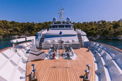 A luxurious white yacht is anchored in a calm bay with lush green hills in the background.