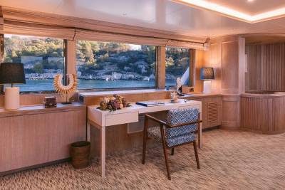 A serene workspace with a desk and chair overlooks a tranquil bay surrounded by lush green hills.