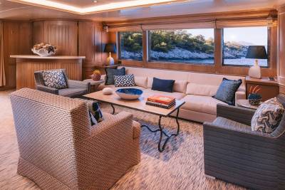 Relax in this luxurious yacht salon with stunning views of the rocky coastline and serene blue waters.