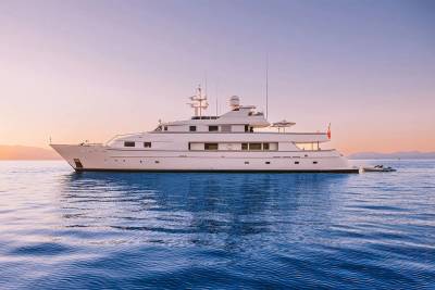 A sleek white yacht glides across calm blue waters under a soft pastel sky.