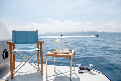 A refreshing pitcher of lemonade and glasses await on a small table beside a director's chair on a boat, with water skiers in the distance.