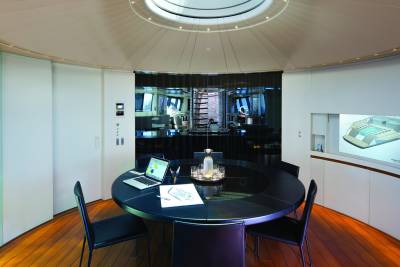 A sleek, modern conference room on a luxury yacht features a circular table, a laptop, and a projected architectural rendering.