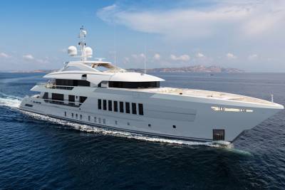A sleek, modern superyacht glides through the deep blue ocean under a bright, cloudy sky.