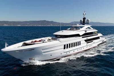 A sleek white superyacht glides through the deep blue sea under a clear sky, with a distant coastline visible.