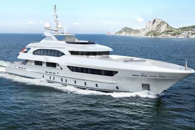 A sleek white yacht cruises through the deep blue sea with a picturesque mountainous coastline in the background.