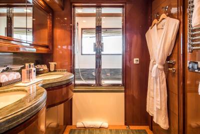 Luxurious white bathrobes hang beside a heated towel rack in this opulent yacht bathroom.
