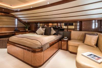 Luxurious yacht stateroom features a plush bed, elegant wood finishes, and a comfortable leather sofa.
