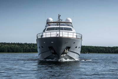 A sleek grey yacht cuts through calm blue waters with a lush green forest lining the horizon.