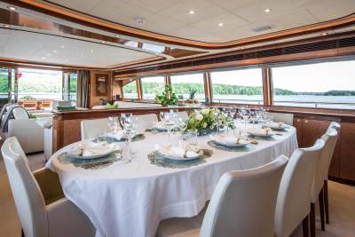 A formal dining table set for a feast awaits guests aboard a luxurious yacht with panoramic water views.