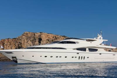 A sleek white yacht glides through calm blue waters against a backdrop of rugged, sun-drenched cliffs.