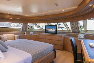 Luxurious yacht cabin features a comfortable bed, entertainment center, and a desk with a view of the rocky coastline.