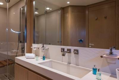 A modern bathroom features a sleek sink and shower area with warm wood accents and polished chrome fixtures.